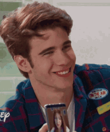 a young man is smiling while holding a cell phone with a patch that says " on the air " on it