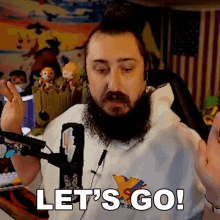 a man with a beard is sitting in front of a microphone and saying let 's go !