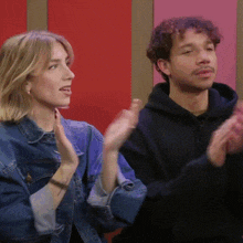 a man and a woman are clapping in front of a pink wall