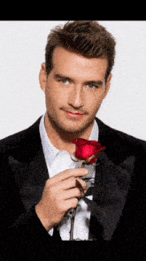 a man in a tuxedo holds a red rose
