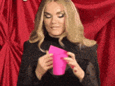 a woman in a black dress is holding a pink cup in her hands .