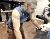 a man in a blue tank top is kneeling down in front of a laptop .