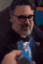 a man with glasses and a beard is sitting on a couch eating a snack .