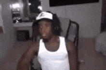 a man wearing a white tank top and a hat is sitting in a chair in a room .