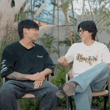 a man wearing a dior tears shirt sits next to a man wearing a black shirt