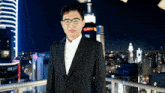 a man in a suit and glasses stands on a balcony overlooking a city