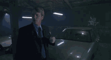 a man in a suit and tie is pointing at a car in a dark garage