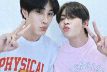 two young men are standing next to each other and making funny faces while giving peace signs .