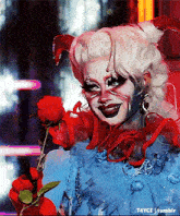 a drag queen is holding a red rose in her hand .