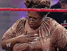 a woman wearing glasses is standing in a wrestling ring holding her chest .