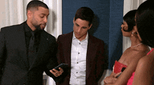 a man in a suit is looking at his phone while standing next to two women