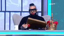 a man sitting at a desk with a crown on it and the word sport on the bottom right