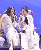 two women are sitting next to each other and one of them is holding a microphone with the letter t on it