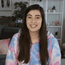 a woman wearing a tie dye hoodie is smiling