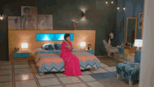 a woman in a pink dress is sitting on a bed