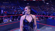 a woman in a black dress is standing in a wrestling ring with a crowd watching .