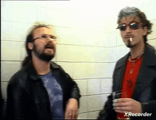 two men are standing next to each other and one is smoking a cigarette while the other is holding a glass of wine ..