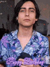 a young man in a floral shirt is holding a cell phone in his hand .
