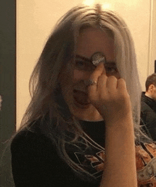 billie eilish is wearing a black shirt and a ring and covering her face with her hand .