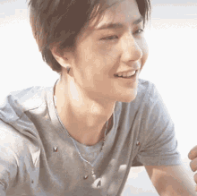 a young man wearing a grey shirt and a blue necklace smiles for the camera