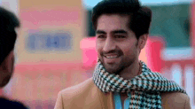 a man wearing a scarf and a jacket is smiling and talking to another man .