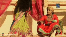 a man in a red costume sits next to a woman in a green dress on a sony television show