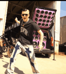 a man is standing in front of a motorcycle and a van with a purple speaker box in the back