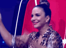 a woman in a leopard print shirt is sitting in a red chair with her hands in the air .