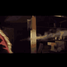 a woman in a red jacket is standing in a dark room with smoke coming out of a window