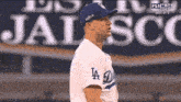 a man wearing a la dodgers jersey stands in front of a jalisco sign