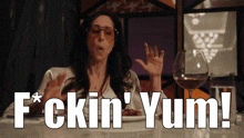 a woman sitting at a table with a plate of food and a glass of wine with the words f * ckin ' yum !