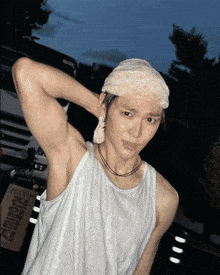 a man wearing a bandana and a white tank top stands in front of a sign that says ' parking ' on it