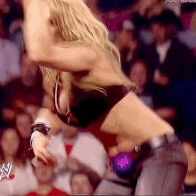 a female wrestler is dancing in front of a crowd while wearing a purple belt with the letter w on it .