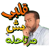 a man with a beard has his hand on his chin in front of a sign that says قلبي