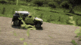 a car is driving down a dirt road with grass in the background