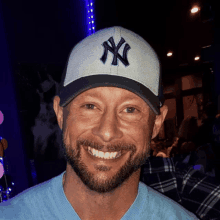 a man with a beard wears a ny hat