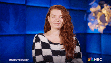 a woman in a black and white checkered sweater with the nbc logo on the bottom