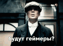 a man in a suit and hat stands in front of a sign that says " будут геймеры "