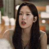 a woman with long hair is sitting at a table with her mouth open and looking at the camera .