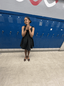 a girl in a black dress is standing in front of a wall of blue lockers