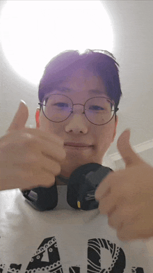 a young man wearing glasses and headphones giving a thumbs up