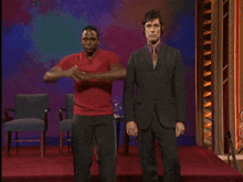 a man in a suit stands next to a man in a red shirt on a stage