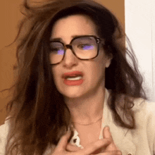 a woman wearing glasses and a white jacket is making a face .
