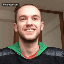 a man with a beard is smiling and wearing a green jacket .