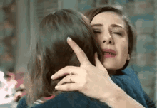 a woman is hugging another woman who is crying and holding her face .