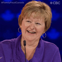 a woman in a purple shirt is smiling in front of a microphone with the hashtag #familyfeudcanada
