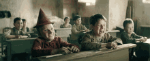 a group of children are sitting at desks in a classroom and one of them is wearing a witch hat