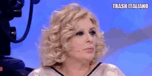 a woman with blonde curly hair is sitting in front of a camera with the words trash italiano written above her .