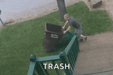 a man is pushing a trash can down a sidewalk next to a railing .