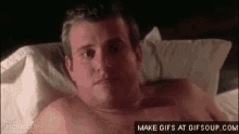 a shirtless man is laying in a bed with a white blanket .